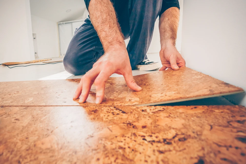 Homme installant du parquet en bois dans une pièce blanche, agenouillé sur le sol, positionnant des lames de parquet avec ses mains