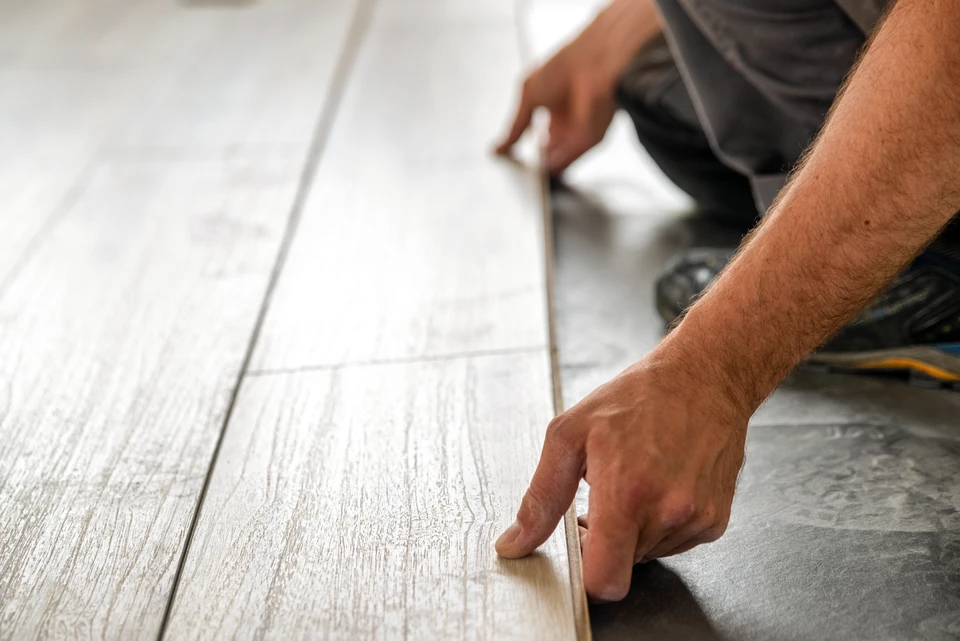 Artisan en tenue orange installe un parquet en lames de bois clair dans une pièce résidentielle