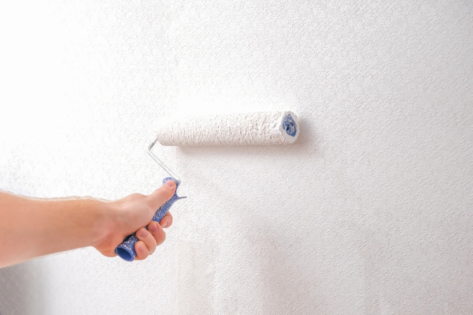 Ouvrier en bâtiment applique de la peinture blanche sur un mur intérieur à l'aide d'un rouleau à manche télescopique