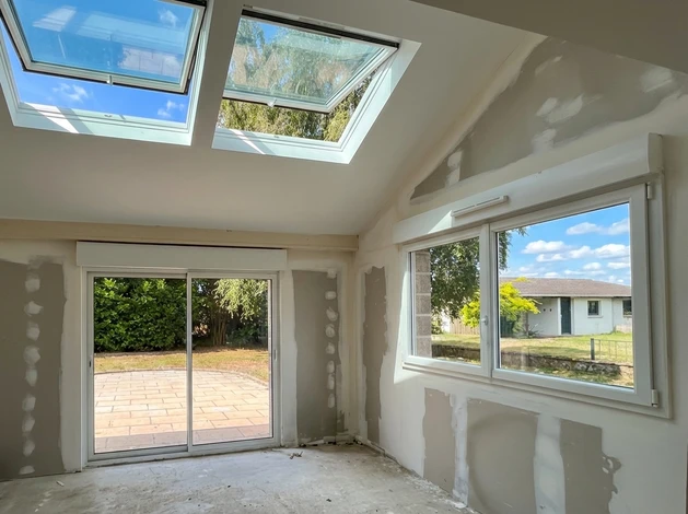 Un peintre en bâtiment applique de la peinture blanche sur un mur intérieur à l'aide d'un rouleau à peinture